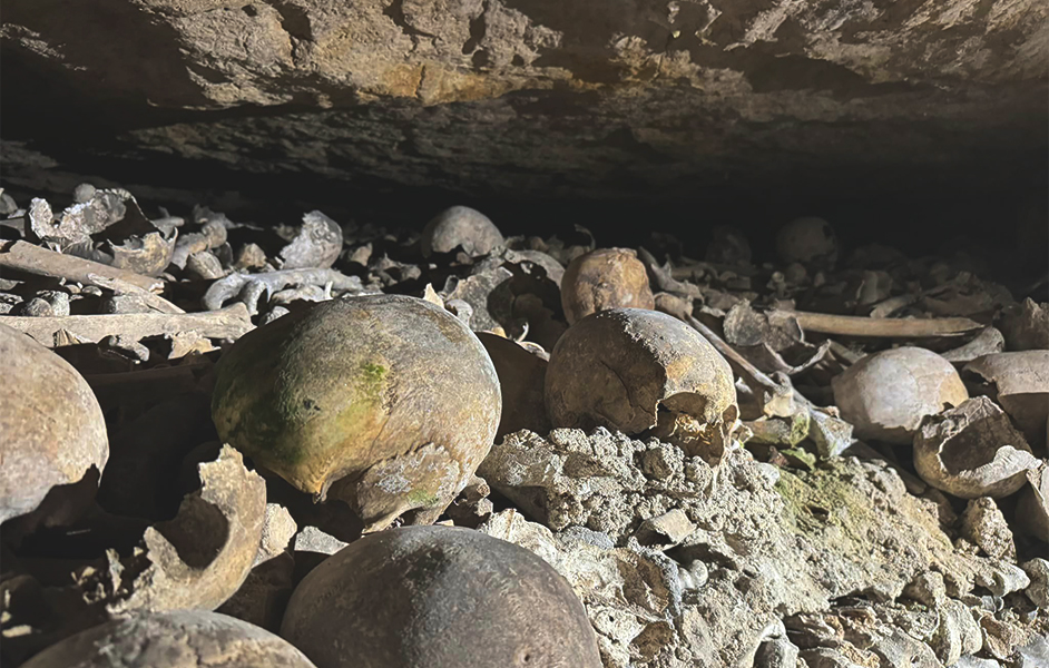 Dimly lit tunnel in the Paris Catacombs filled with skeletal remains